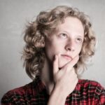 Portrait of a young adult with curly blond hair, deep in thought indoors.