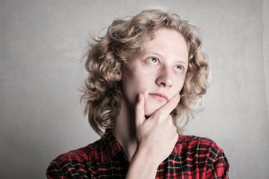 Portrait of a young adult with curly blond hair, deep in thought indoors.