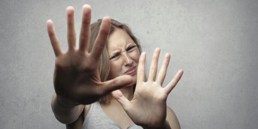 Portrait of a fearful woman in a gray tank top with hands pushed forward against a gray background.