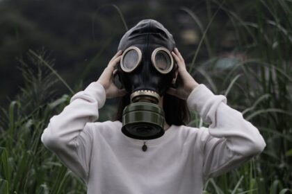 Individual wearing a gas mask standing in tall grass, symbolizing protection from toxins.
